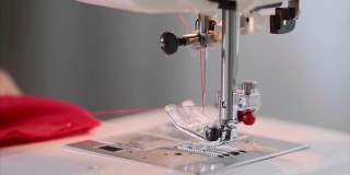 女裁缝的双手在缝纫机上缝红衣服直缝。