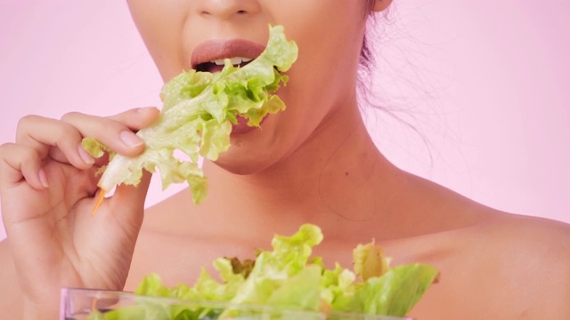 年轻快乐的女人吃着粉色背景上的健康沙拉。清洁平衡的健康食品理念。健康饮食与健身理念。有机食品。医疗保健理念。视频:多样化的肖像