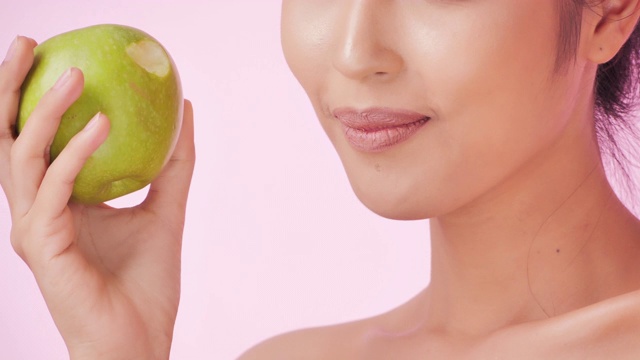 年轻快乐的女人在粉红色的背景下吃苹果。清洁平衡的健康食品理念。健康饮食与健身理念。有机食品。医疗保健理念。视频:多样化的肖像