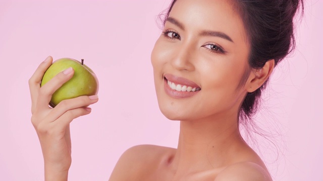 美丽的女人肖像与苹果在粉红色的背景。清洁平衡的健康食品理念。健康饮食与健身理念。有机食品。医疗保健理念。视频:多样化的肖像