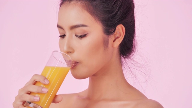 年轻快乐的女人喝橙汁在粉红色的背景。清洁平衡的健康食品理念。健康饮食与健身理念。有机食品。医疗保健理念。视频:多样化的肖像