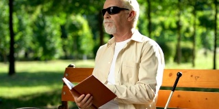 戴墨镜的盲人厌倦了阅读盲文，坐在公园里