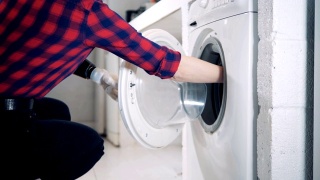 一名妇女戴着机器人假肢往洗衣机里装东西。视频素材模板下载