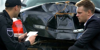 一名男警官用平板电脑拍下了被损坏的汽车，悲伤的司机看起来像被撞坏了的汽车