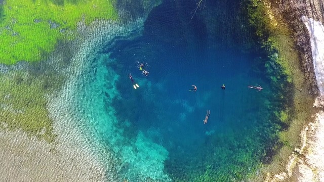 Top view of a clear cold blue lake. Divers in suits swim in clear, clear water. Water with blue minerals aerial view.