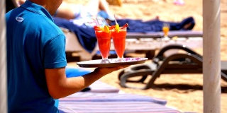 侍者在埃及海滩上斟酒。侍者端着一个盛着热带果汁的托盘