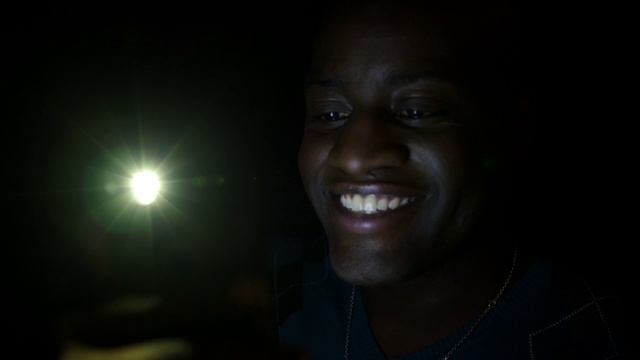 深色皮肤的男人在晚上用手机对着4K相机微笑