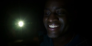 深色皮肤的男人在晚上用手机对着4K相机微笑