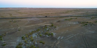 日落时分，汽车在沙漠中间的空旷道路上行驶的鸟瞰图