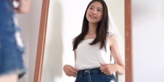 年轻美丽的亚洲女人看着镜子后，穿衣服，她检查身体，为准备下一个旅行旅行的夏天在酒店房间4k决议。