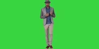 时髦的积极乐观的人穿着休闲衬衫和太阳帽行走和交谈的绿色屏幕，色度键
