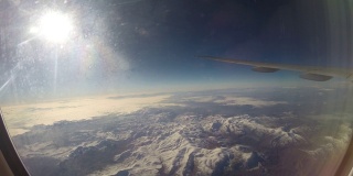 透过飞机窗户观看雪山上空的飞机机翼