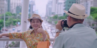 一位老人在阳台上与粉丝们合影，以泰国首都为背景。