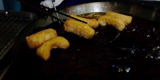 当地市场，厨师在热煎锅中制作油条，传统的油条食品。中国的煎饼。多莉拍摄