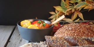 女人的手把塞满辣椒、肉末、米饭和玉米的碗放在木桌上。秋天的热的食物。