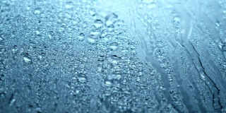 近距离观看水滴落在玻璃上。雨打在窗户上。雨季，秋天或春天。雨滴滴落，深蓝色的天空。特写，柔焦。