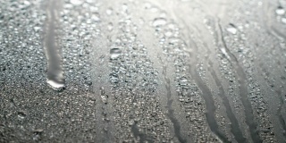 近距离观看水滴落在玻璃上。雨打在窗户上。雨季，秋天或春天。雨滴滴落，灰色的天空。特写，柔焦。
