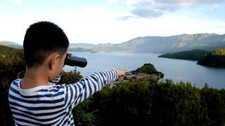 亚洲男孩用双筒望远镜看泸沽湖视频素材模板下载