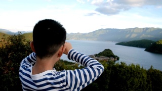 亚洲男孩用双筒望远镜看泸沽湖视频素材模板下载
