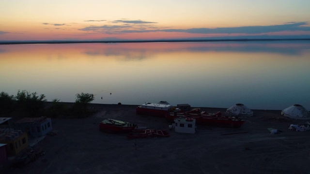 鸟瞰蒙古包，船只和人们在日落时游泳在一个湖泊，中国新疆