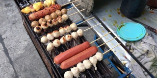 泰国街头小吃市场，摊贩的手在木炭炉上烤着肉丸、猪肉丸子和香肠。烹饪概念。视频片段。
