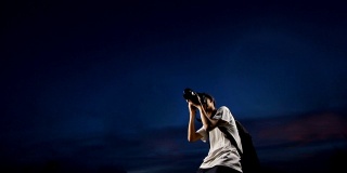 一个年轻人拿着相机，在晚上拍星星的照片