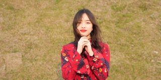 这是一幅美丽的中国年轻女子的肖像，她穿着红色的裙子看着镜头，以绿色的草地为背景做着祈祷的手势。