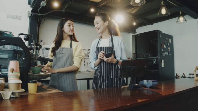 年轻美丽的亚洲女咖啡师穿着围裙在咖啡厅的柜台接受顾客的电话订购咖啡面带微笑。咖啡店和小型咖啡店的概念。