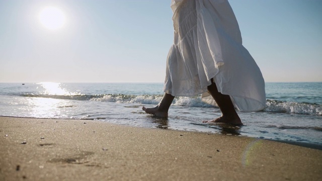 穿着白色裙子的女孩赤脚走在海边的海浪上