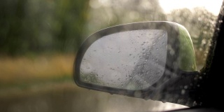 雨点落在挡风玻璃上，落在背景侧后视镜上。