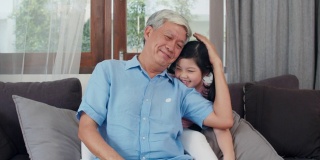 亚洲爷爷在家休息。高三的中国，爷爷开心的放松和小孙女女孩享受闭眼惊喜一起在客厅玩的概念。慢动作镜头。