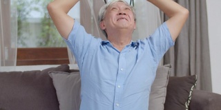 亚洲老年人在家玩游戏。亚洲老年中国男性快乐乐趣与虚拟现实，躺在家里客厅沙发上玩虚拟现实游戏的概念。慢动作镜头。