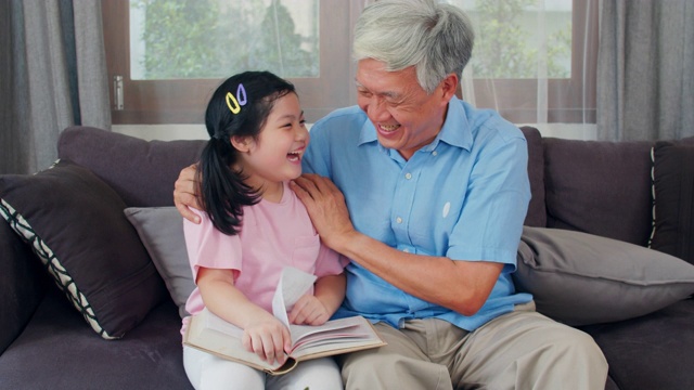 亚洲爷爷在家休息。高三语文，爷爷开心的和小孙女女儿一起享受在客厅看书和做作业的概念。慢动作镜头。