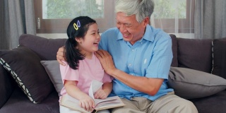 亚洲爷爷在家休息。高三语文，爷爷开心的和小孙女女儿一起享受在客厅看书和做作业的概念。慢动作镜头。