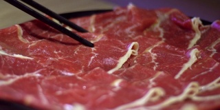 用筷子夹住牛肉生肉的慢动作。北京的中国火锅