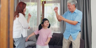 亚洲的祖父母和孙女在家一起听音乐和跳舞。中国老年人，爷爷和奶奶愉快地度过家庭时间和年轻女孩在客厅放松的概念。缓慢的运动。