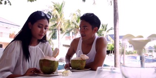 年轻男子与女友在沙滩上野餐，亚洲情侣正坐在、放松和喝着椰子汁的池边。