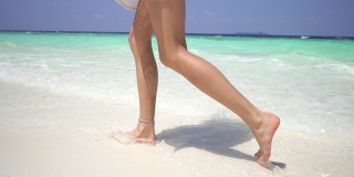 年轻的光着脚的女人走在马尔代夫海岸附近的白色沙滩上。缓慢的运动。