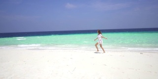 可爱的女孩在马尔代夫岛蔚蓝的海洋附近的白色沙滩上跑步。缓慢的运动。