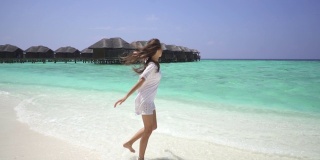 一个女孩在马尔代夫的一个水上小屋附近的白色沙滩上散步并打着漩涡。缓慢的运动。