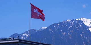 瑞士国旗在阿尔卑斯山脉的背景站在房子的屋顶