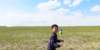 一个亚洲男孩在草原上和风车赛跑