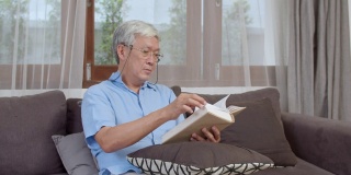 亚洲的老男人在家里放松。亚洲资深华人男性享受休息时间躺在家里客厅的沙发上看书的概念。