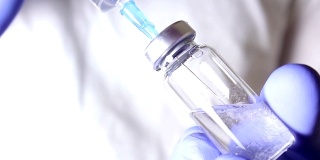 医生用注射器将溶液注射到疫苗小瓶中，混合药物，为注射病人做准备。