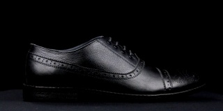 一个时尚的经典黑色鞋与鞋带在黑色的背景旋转。