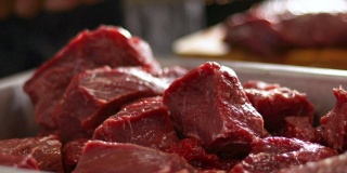烹饪前，厨房里的红色生牛肉块。厨师在模糊的背景上切肉
