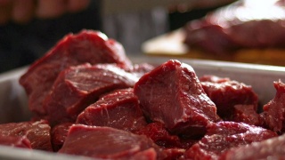 烹饪前，厨房里的红色生牛肉块。厨师在模糊的背景上切肉视频素材模板下载