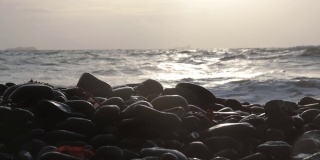 前景的鹅卵石堆叠在海滨，与海浪撞击的背景和波浪溅在卵石在最后。梦幻,环境气氛。