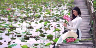 美丽的越南女子手持粉色莲花微笑在大莲花湖的木桥上的肖像，越南，亚洲或东南亚的旅游概念