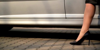 年轻的女士在斑点裙子下了车走在路上的特写。低角度视角与关注女人的腿